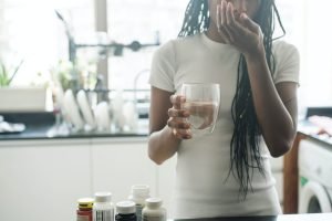 African American woman taking vitamins and supplements at home in her kitchen