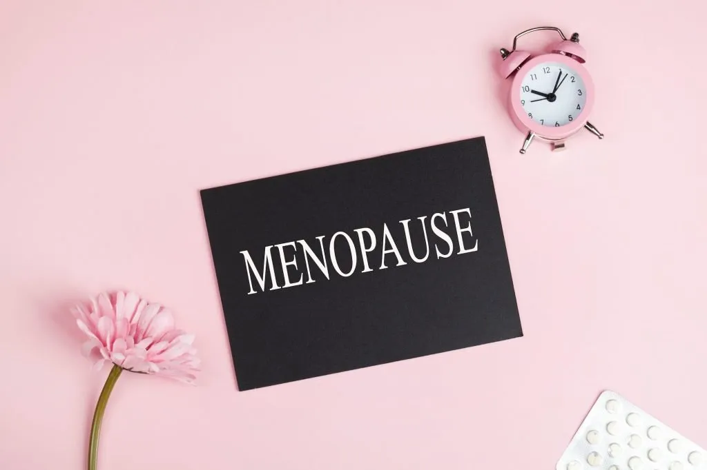 menopause word written on black board, flowers, clock and pills on pink background. women health
